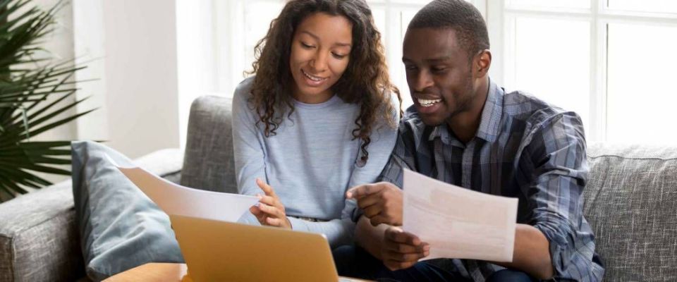 Black married couple sitting on sofa looking at papers and computer