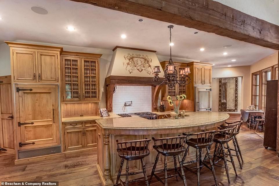 Exquisite: The stone-topped counters are set above light wood cabinets with boiserie, matching a curved kitchen island that is lined with chairs and contains the sink