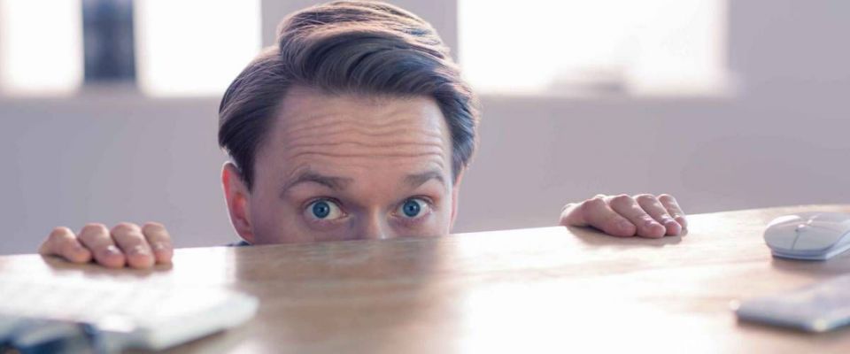 Nervous businessman peeking over desk in his office