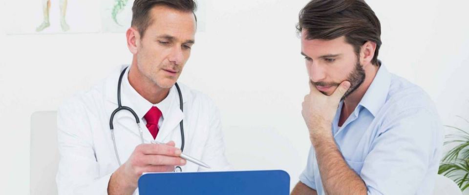 Male doctor discussing reports with patient at desk in medical office