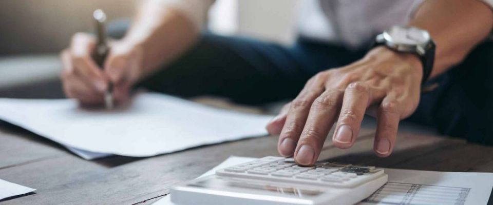 Close up of man&#39;s hands using calculator, writing notes with other hand