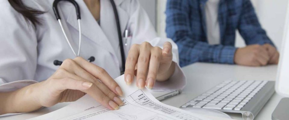 Doctor sitting with young man, looking at forms