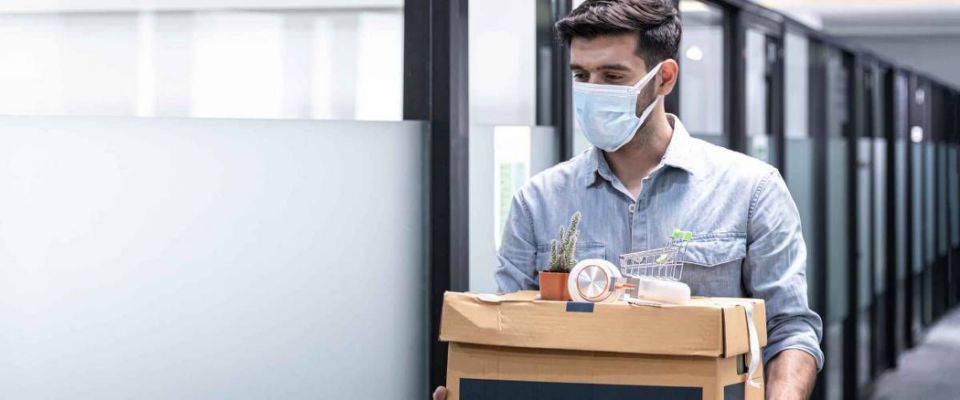 Man walking out of an office holding box of things, wearing a mask