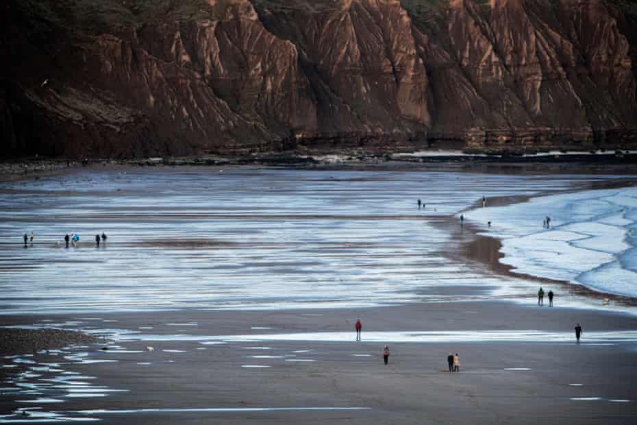 People take a walk along the beach, with Filey Brigg in the background.