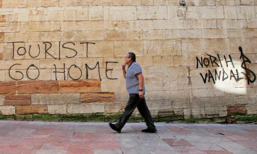 A man walks past a ‘Tourists Go Home’ graffitti on a wall close to the City Hall in Oviedo, northern Spain.