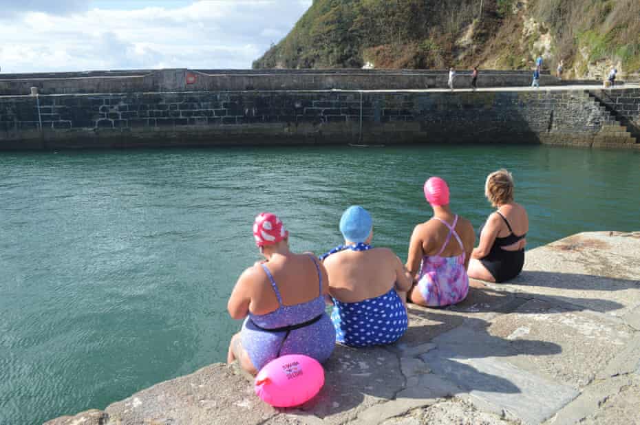 Four swimmers sit on the harbour wall overlooking the sea, near St Austell, Cornwall.