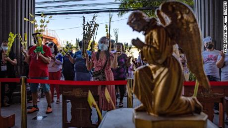 Filipino Catholics wearing facemasks and face shields carry palm fronds as they pray outside a church to celebrate Palm Sunday on March 28, 2021 in Quezon city, Metro Manila, Philippines. 