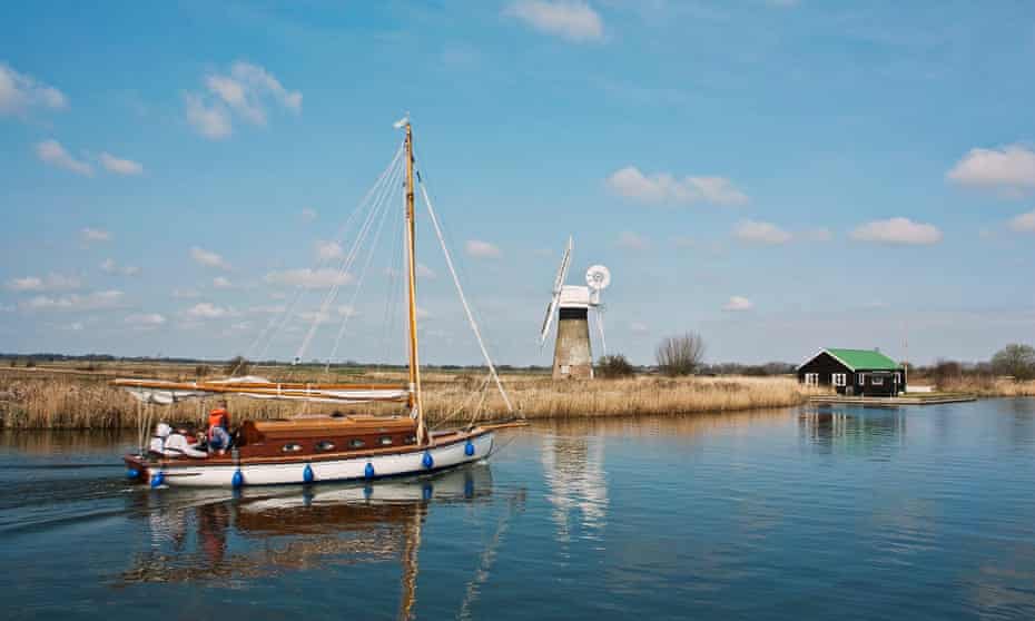 A sail boat meanders along the Norfolk Broads at Thurne