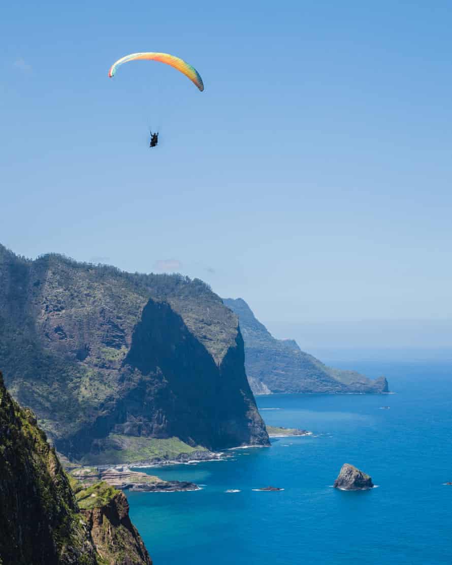 Overview of paraglider flying over Porto da Cruz village with Penha D’aguia mountain as background in Madeira island.