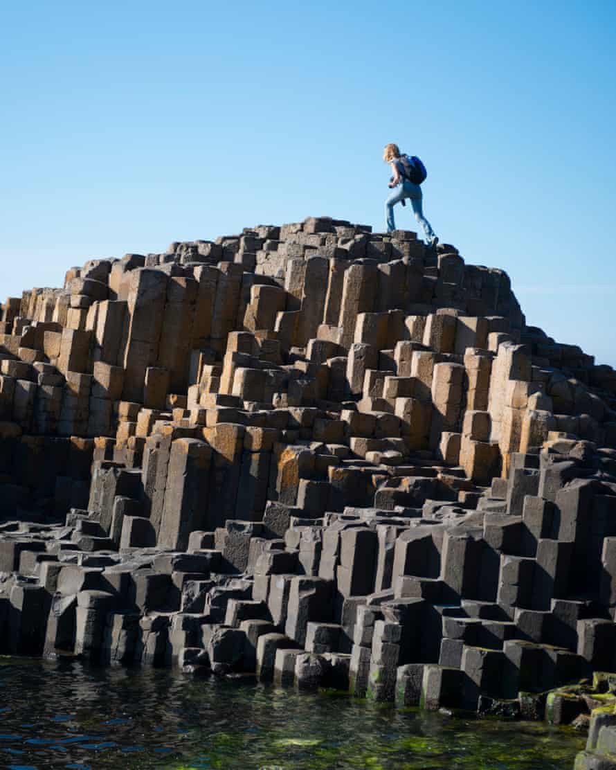 A woman visiting Northern Ireland climbs to the top of a rock outcropping at Giant’s Causeway in Northern Ireland.