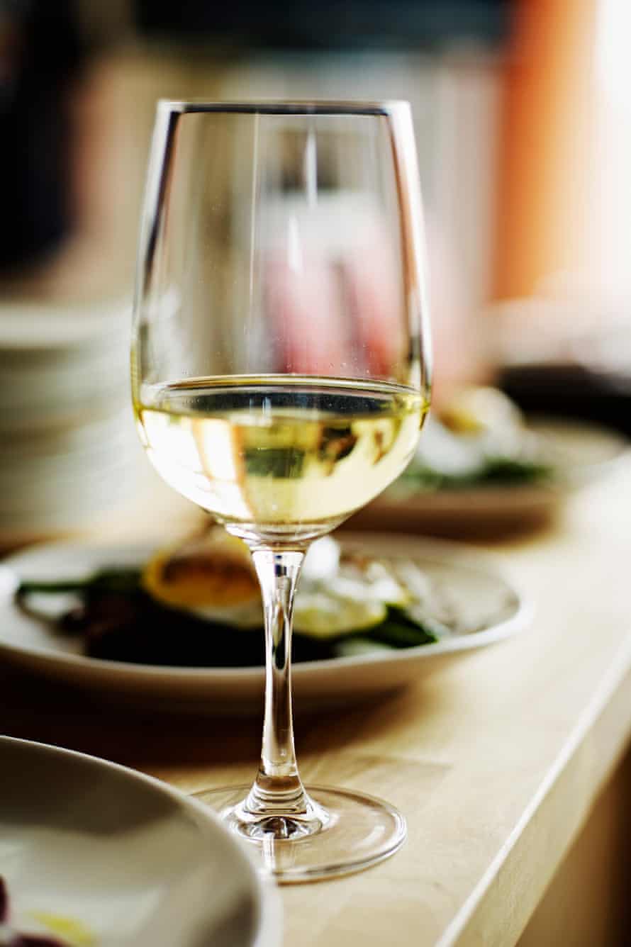 Glass of white wine sitting on countertop with plates of food