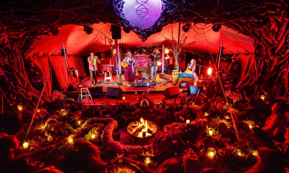 Band performs on a stage, at night, in front of an audience, illuminated by small lanterns, at the Medicine festival in Berkshire, UK, August 2021.