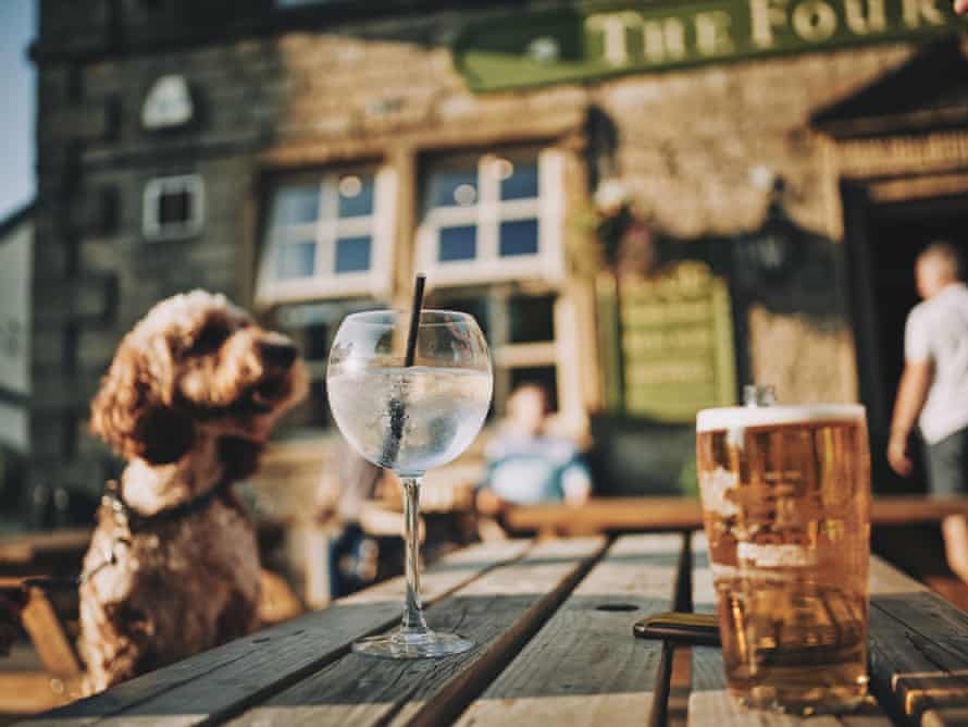 Exterior photograph of The Four Alls Inn, Lancs, UK. A dog is sat on an outside bench looking at a glass of spirits and a pint of beer.